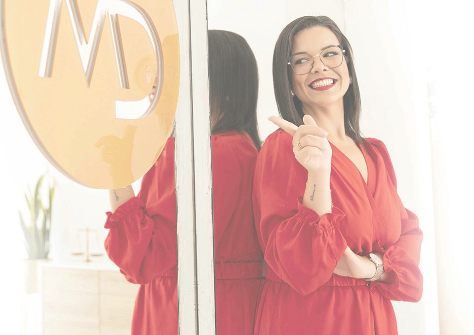 Marina Dourado junto à porta do escritório, com o logótipo MD